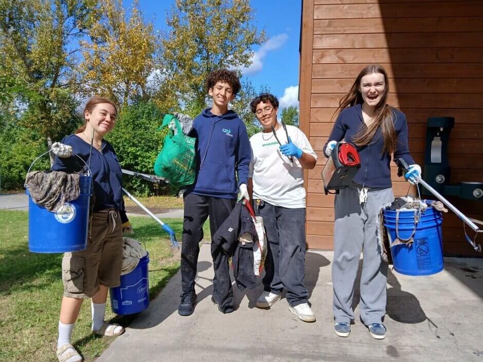 Quatre jeunes brandissent des sacs ou des seaux de déchets en souriant et en riant.