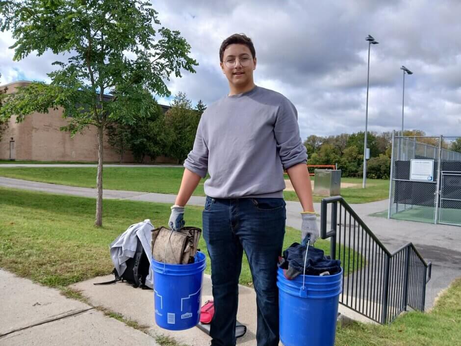 Un étudiant portant deux seaux remplis d'ordures tout en regardant la caméra.