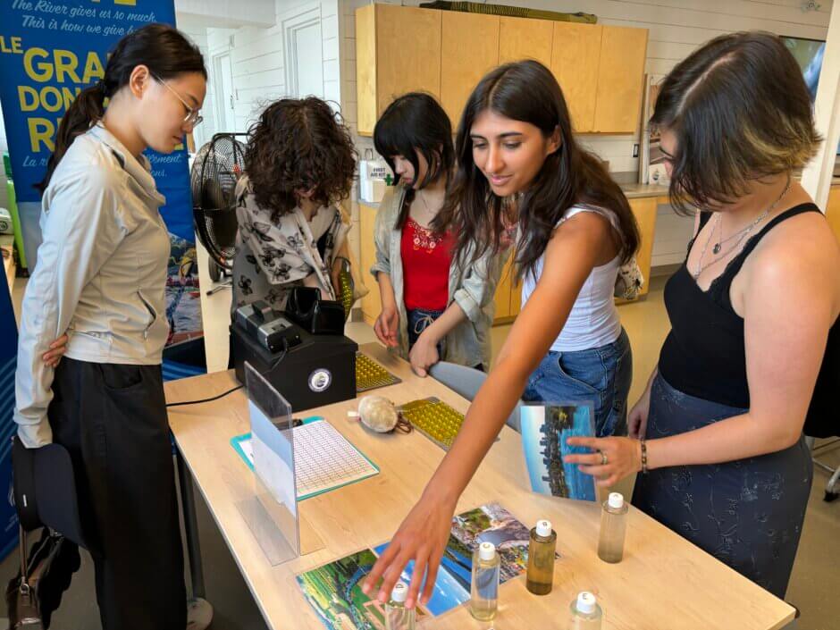 Des jeunes regardent une table du Labo éducatif couverte d'activités et d'informations, y compris des bouteilles de différents types d'eau de rivière.